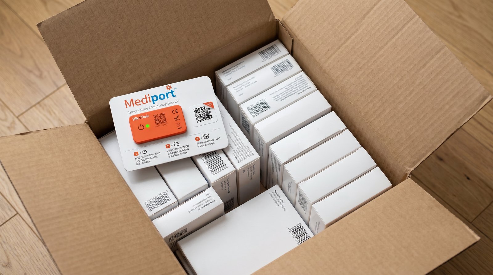 Open shipping box showing stacked pharmaceutical cartons with the Mediport StiknSense card resting on top, LED visible for status check on receipt
